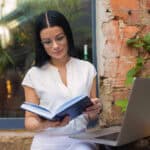 Woman sitting at cafe with book and laptop