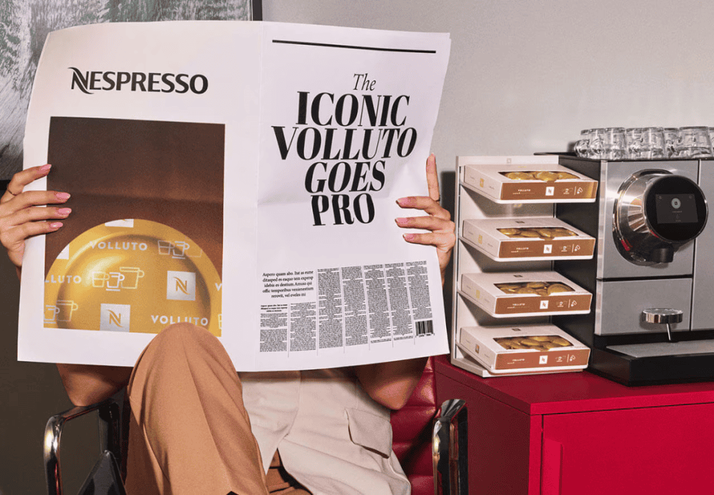 Nespresso Volluto at the office visual with man reading newspaper next to coffee machines and capsules